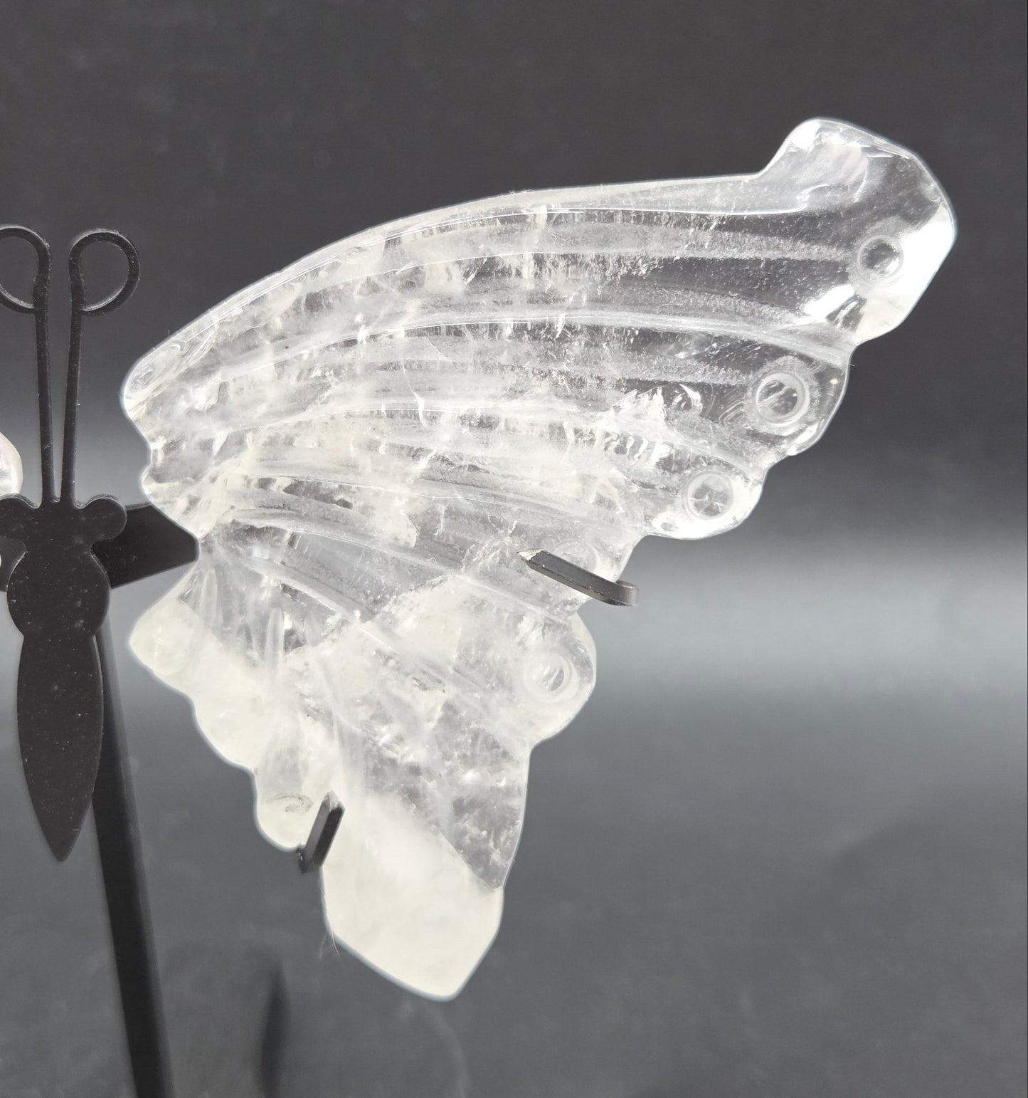 Decorative clear quartz butterfly wings on a black stand on a dark background