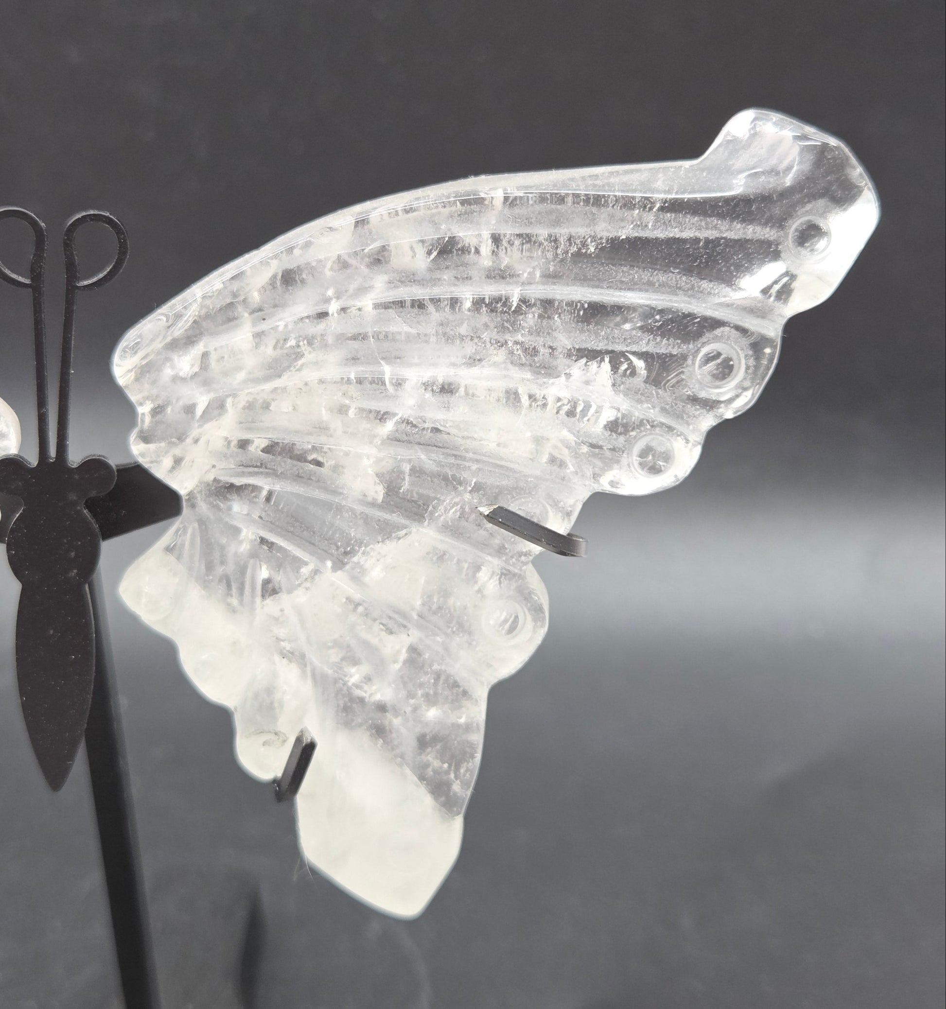 Decorative clear quartz butterfly wings on a black stand on a dark background