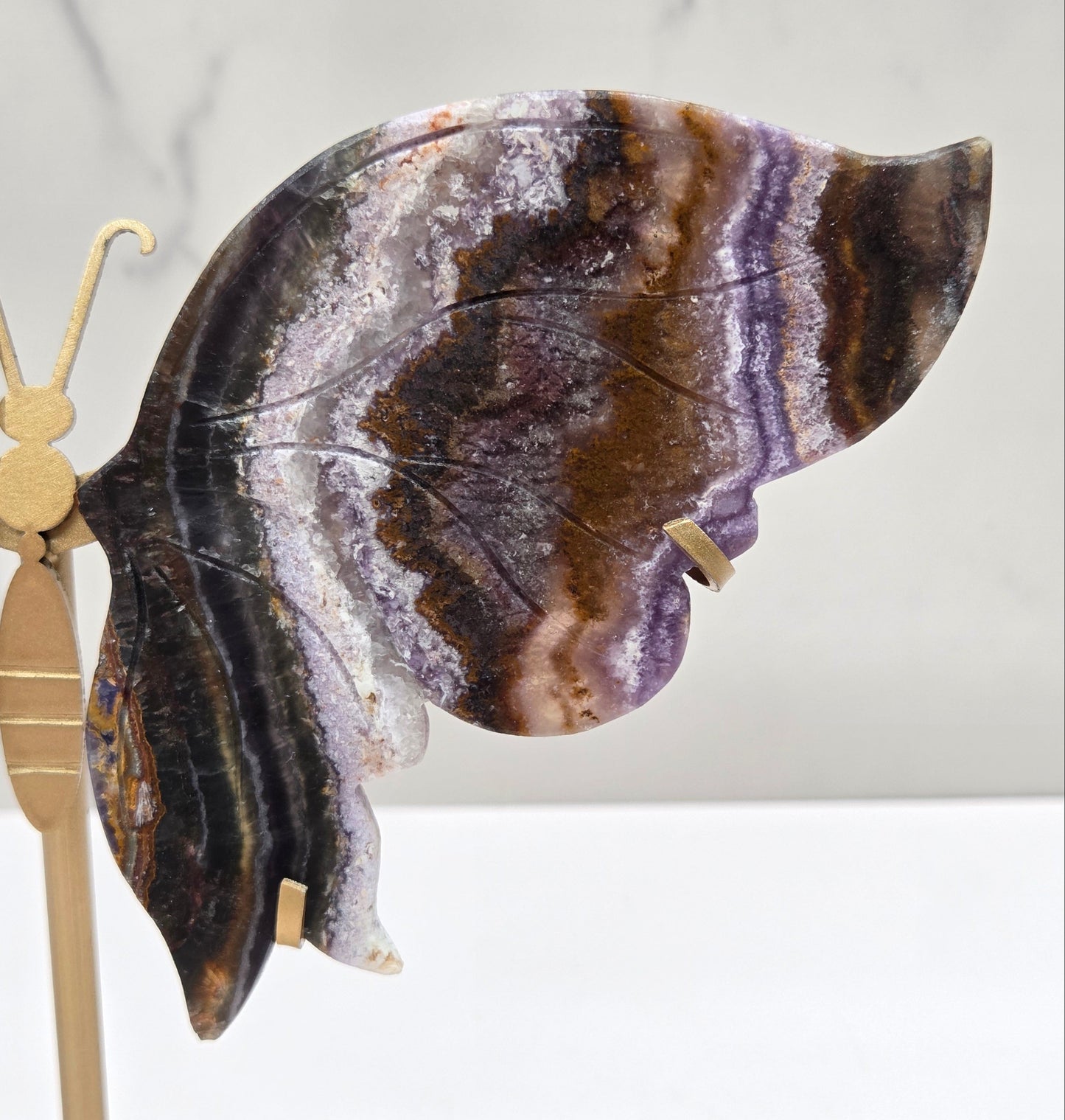 Decorative butterfly with banded crystal wings on a gold metal frame on a marble background