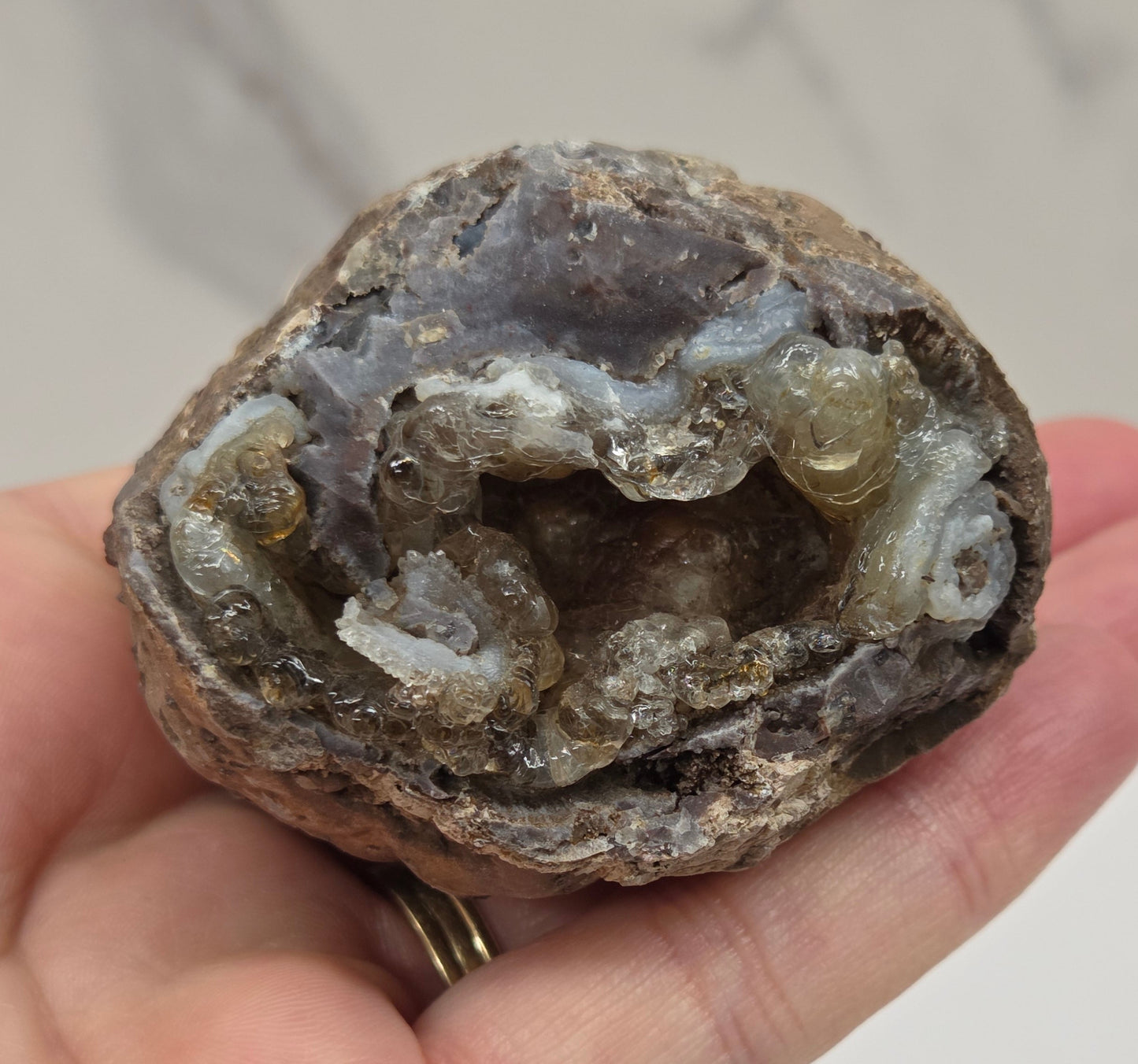 Hand holding a geode with crystals inside against a neutral background