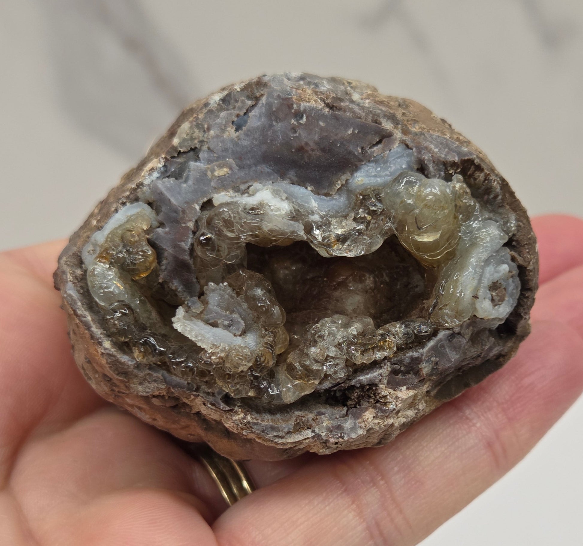 Hand holding a geode with crystals inside against a neutral background