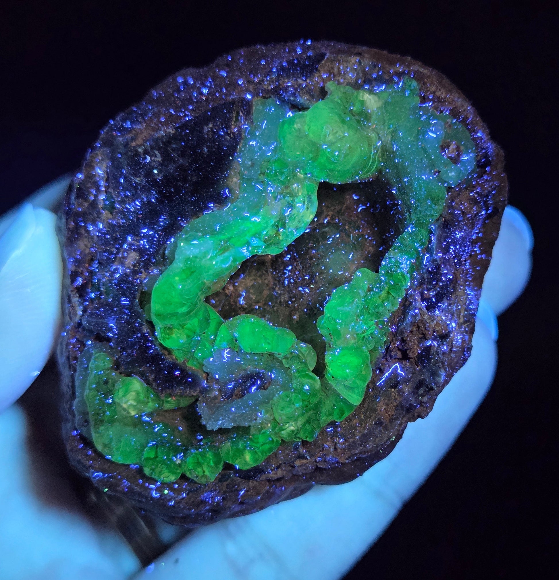 Mineral sample with green fluorescence held by a hand against a dark background