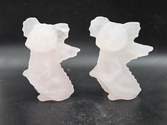 Two pale pink calcite carvings of dragons on a dark surface