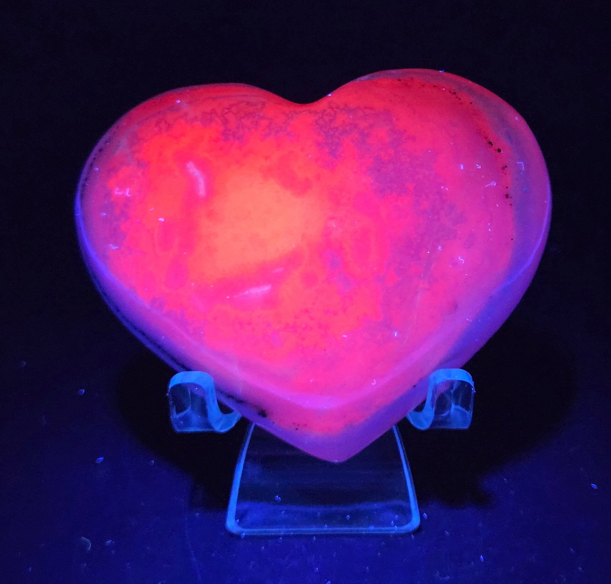 Heart-shaped pink calcite carving under UV light against a dark background