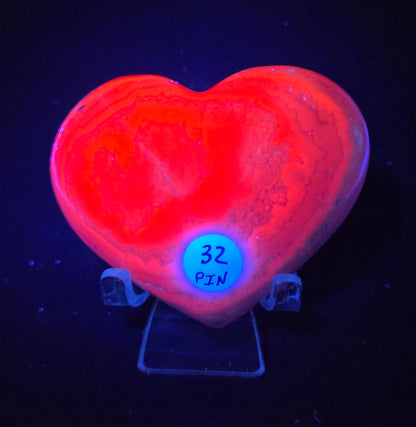 Heart-shaped pink calcite carving under UV light against a dark background