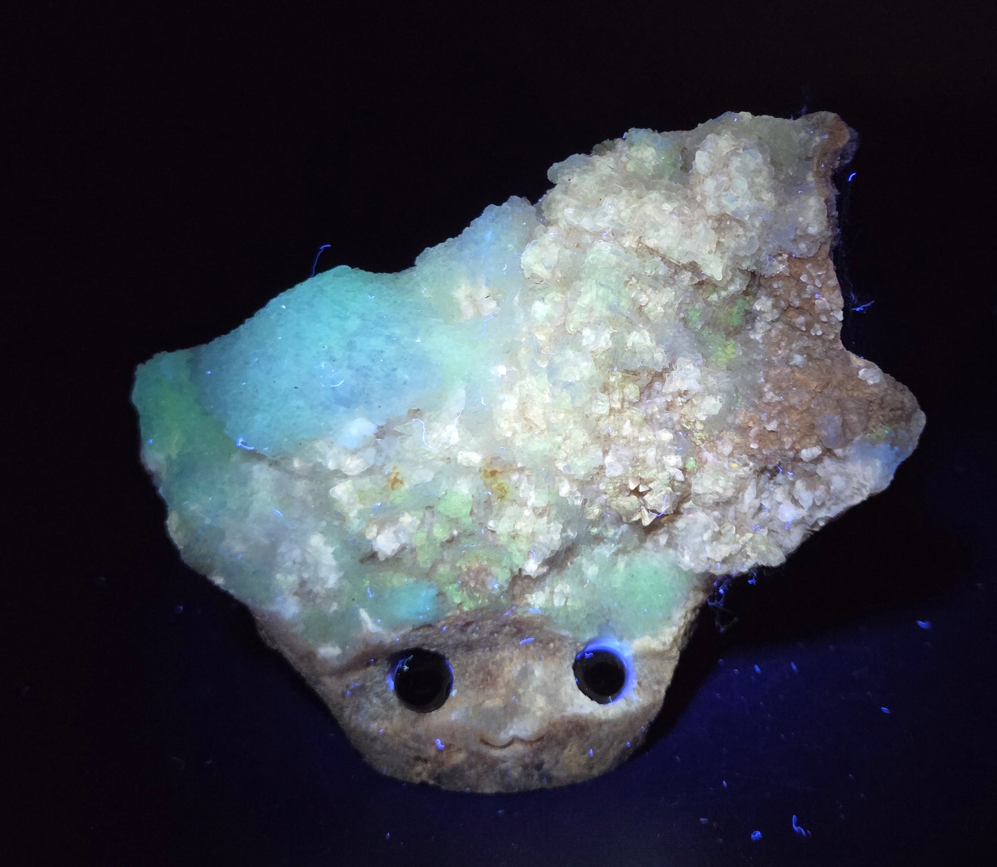 Calcite carved into a groot like carving with eyes and a mouth under UV light