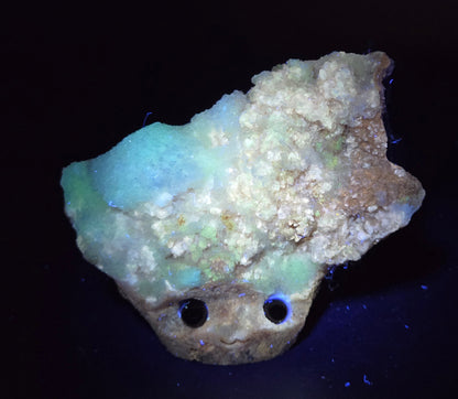 Calcite carved into a groot like carving with eyes and a mouth under UV light