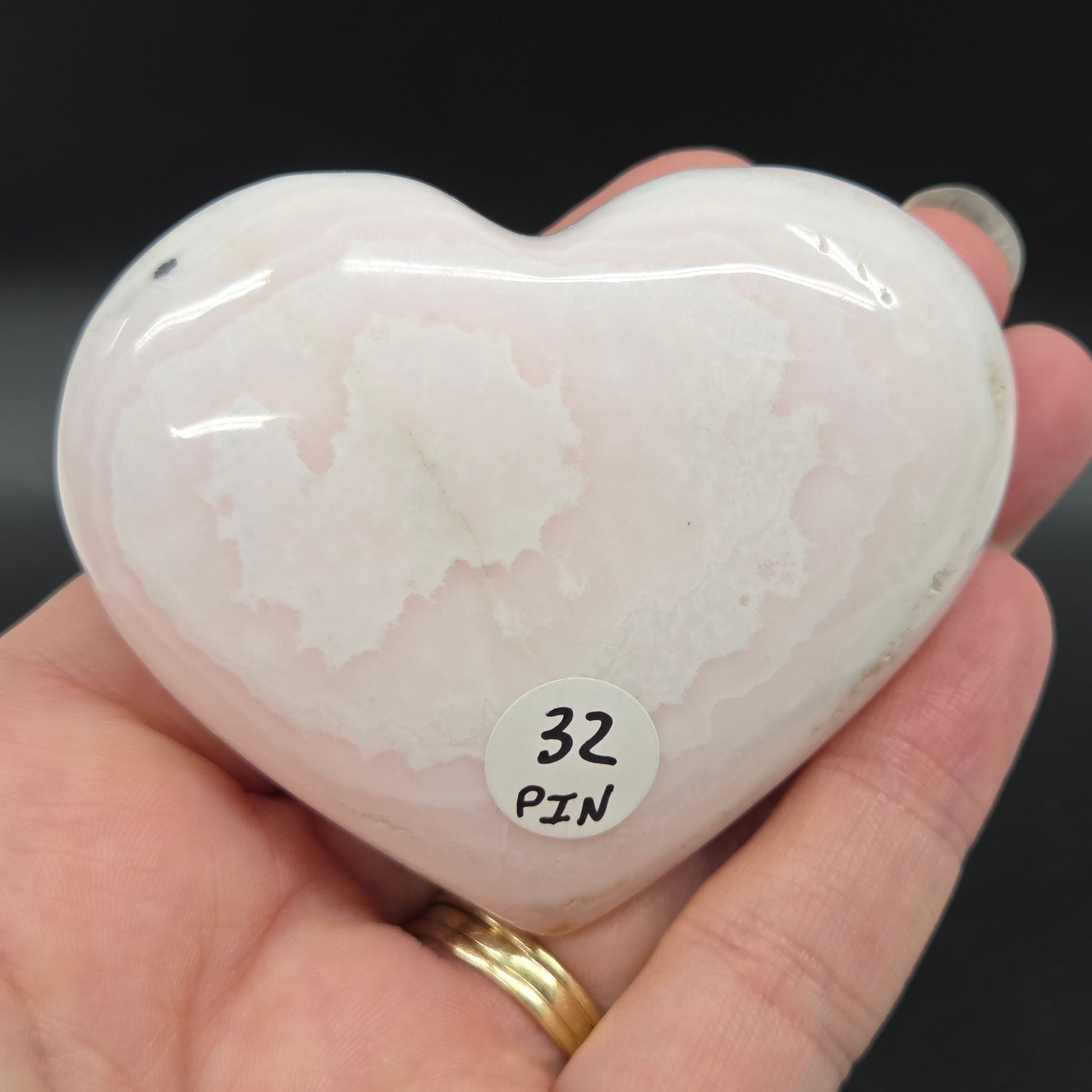 Heart-shaped pale pink calcite carving held in a hand against a dark background