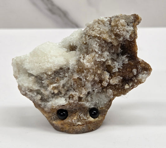 Calcite carved into a groot like carving with eyes and a mouth on a white background