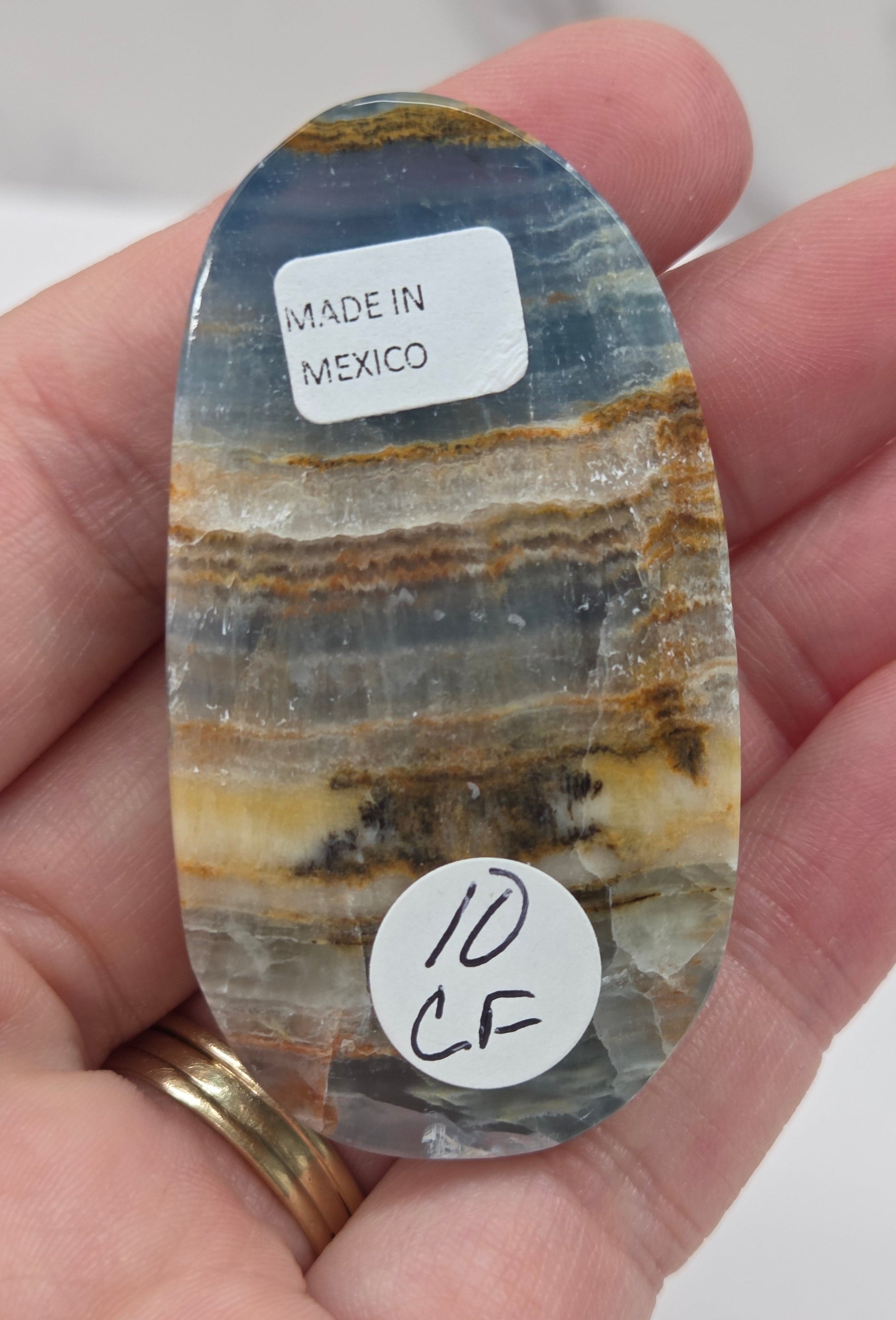 Hand holding a Blue Onyx cabachon stone, displaying various shades of blue and brown.