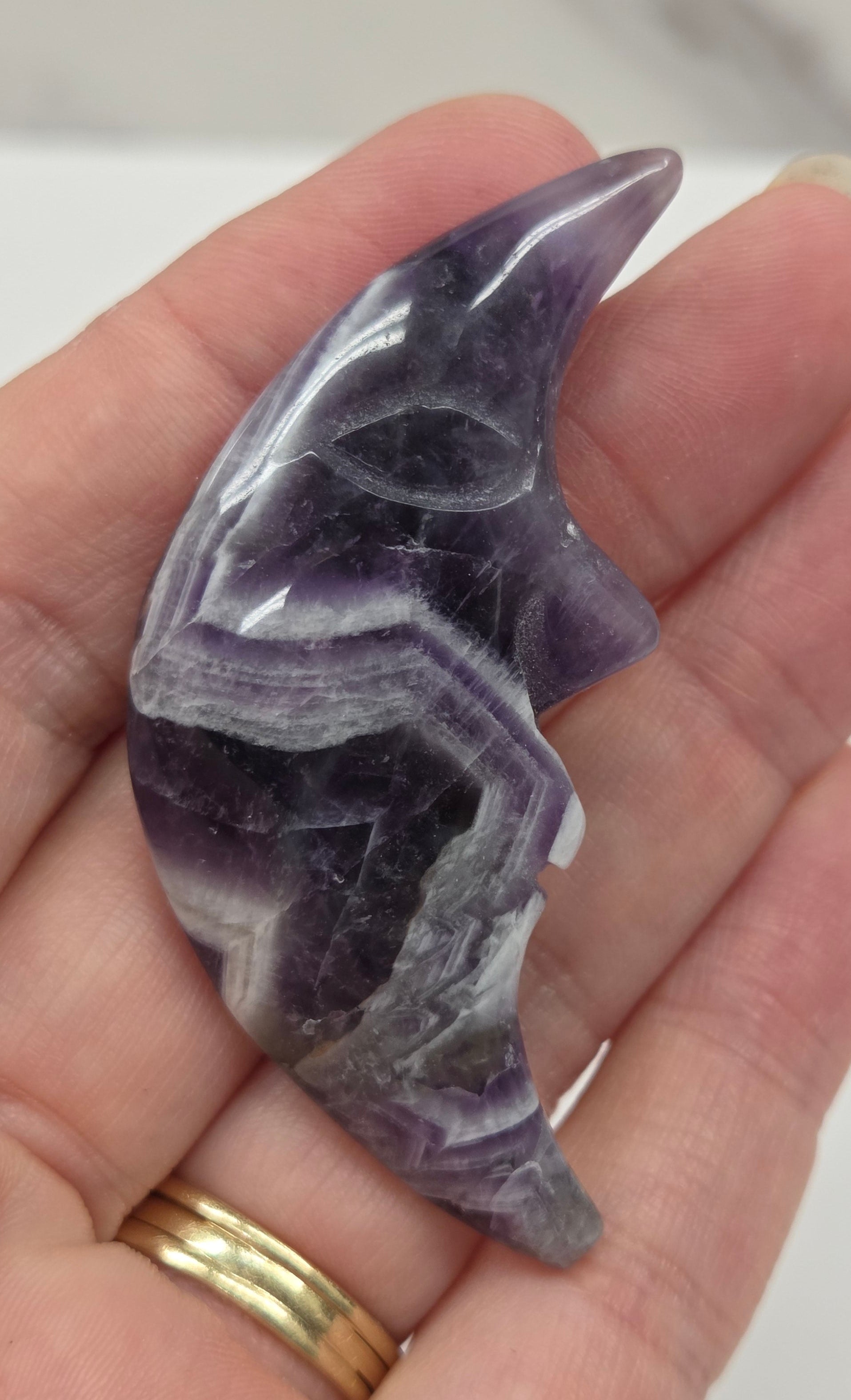 Hand holding a purple and white dream amethyst moon with a face  with a blurred background