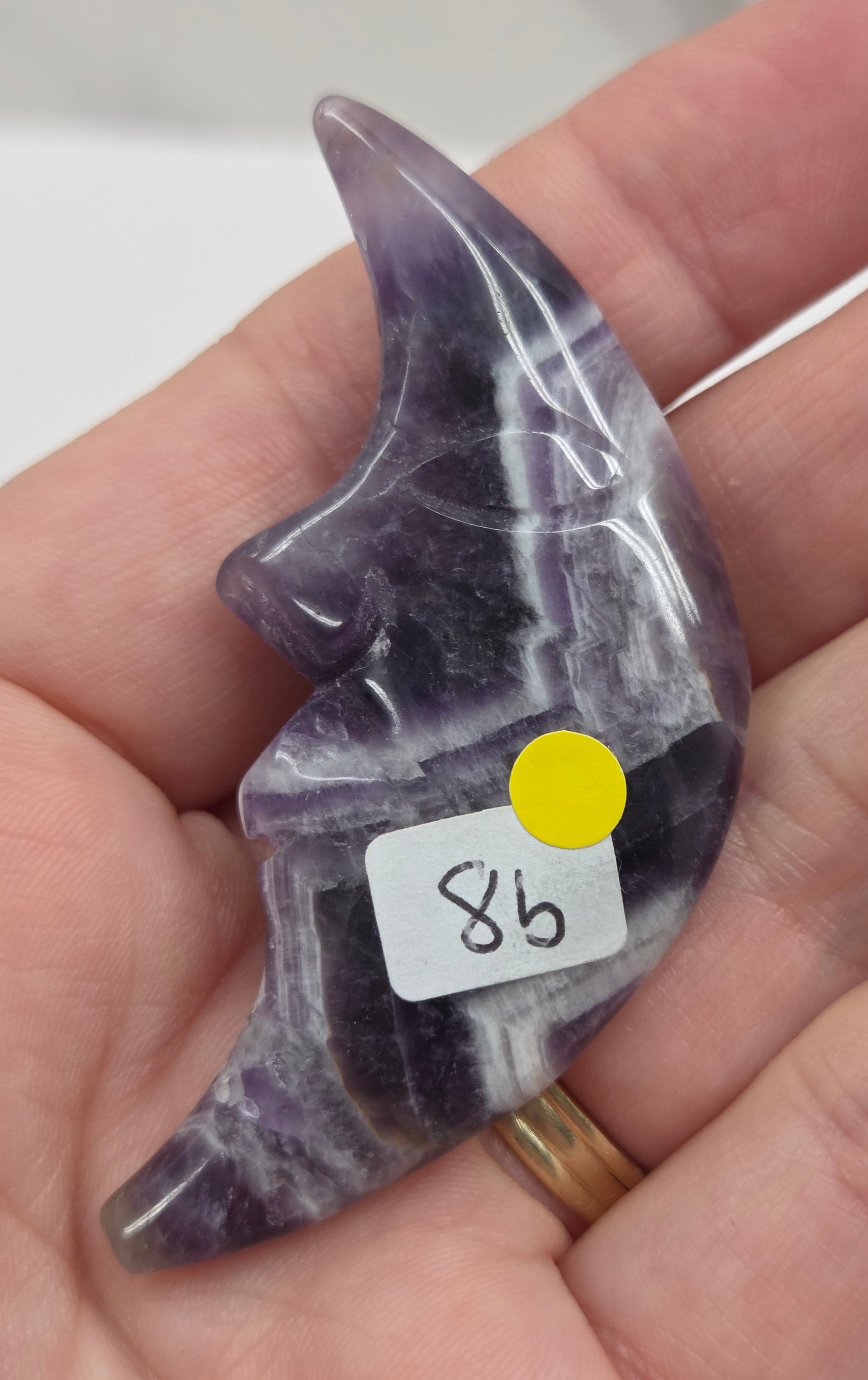 Hand holding a purple and white dream amethyst moon with a face  with a blurred background