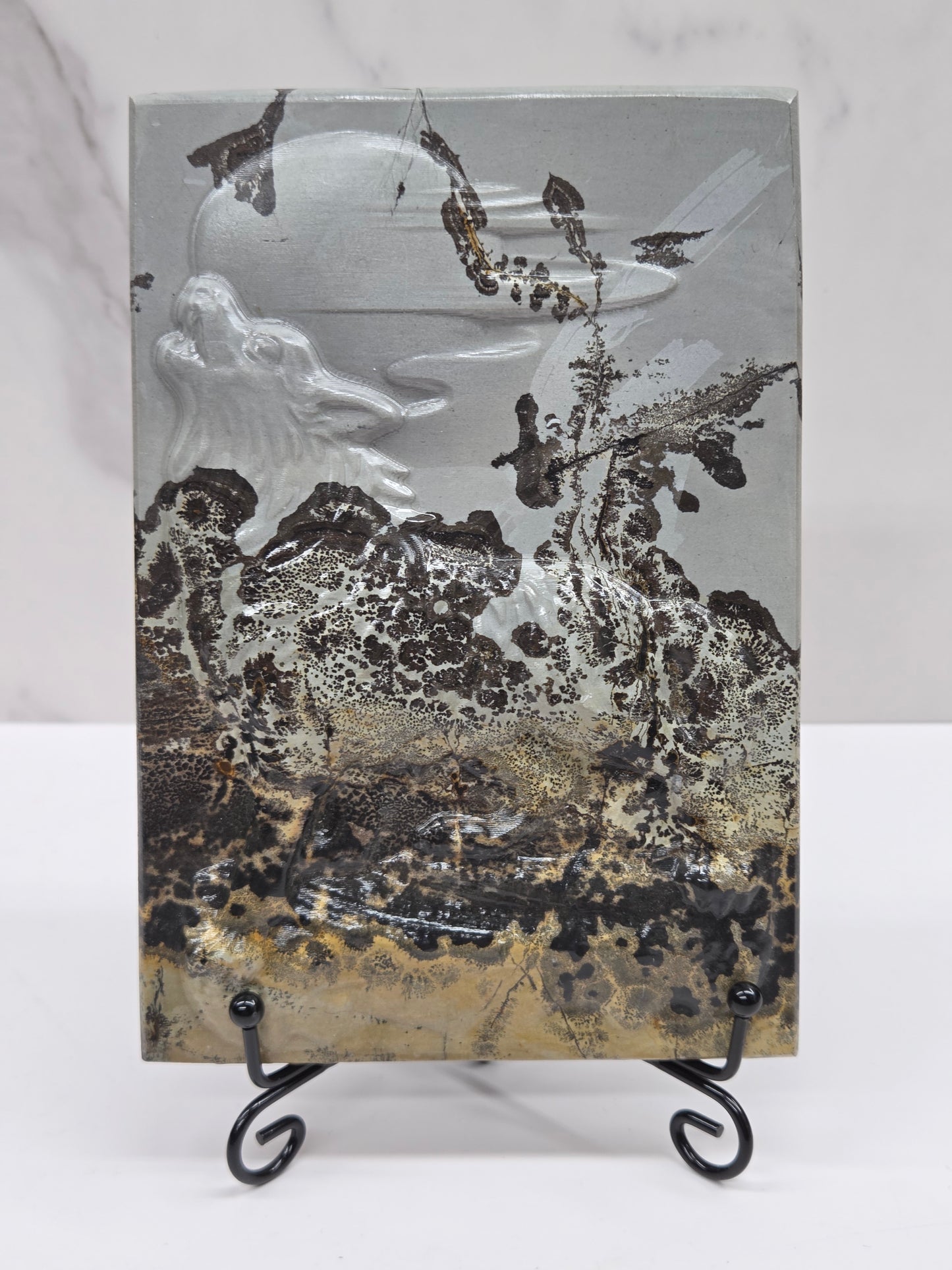 Picture Jasper slab with patterns and a wolf and moon carved into it, on a black stand against a white background