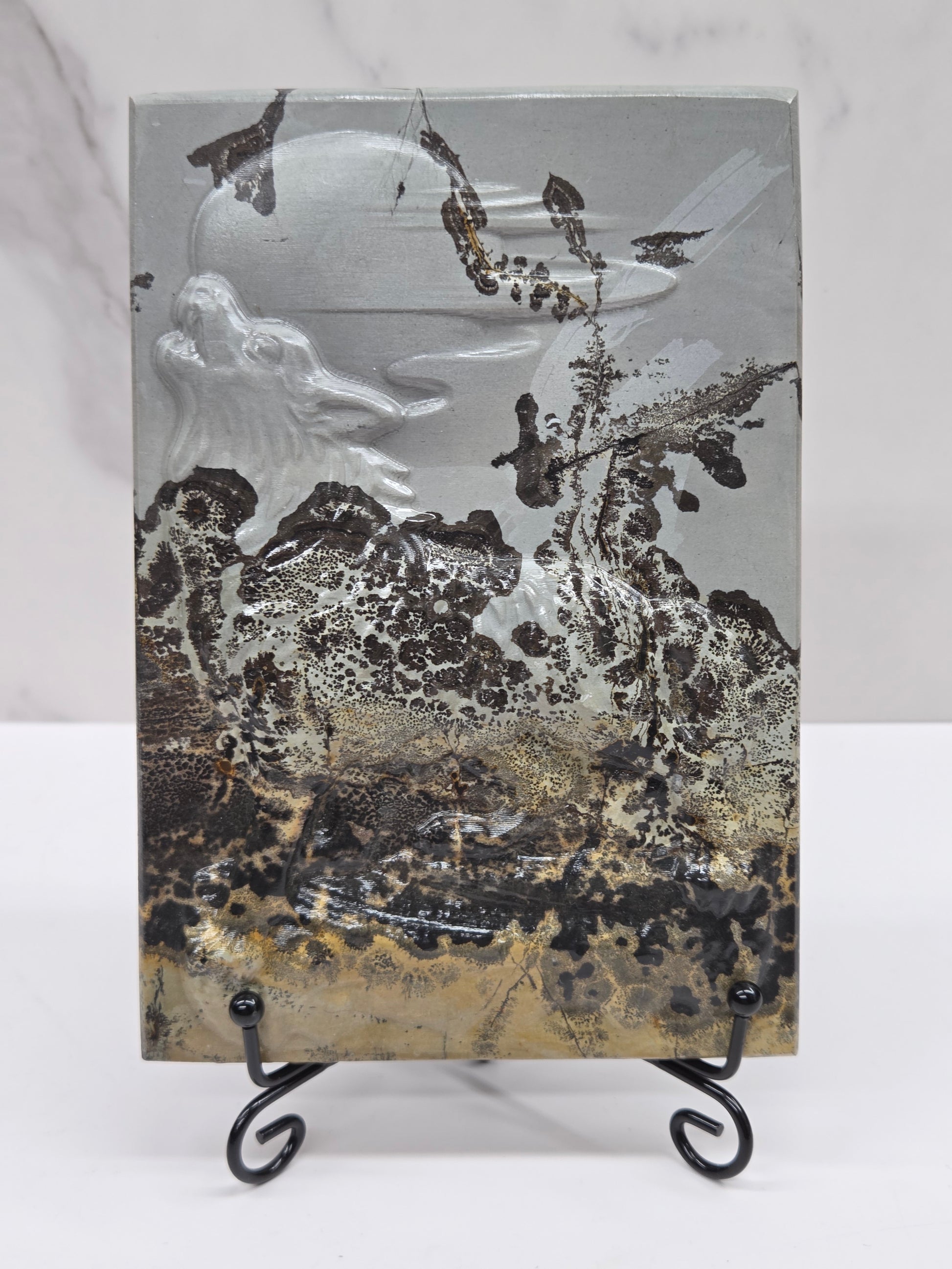 Picture Jasper slab with patterns and a wolf and moon carved into it, on a black stand against a white background
