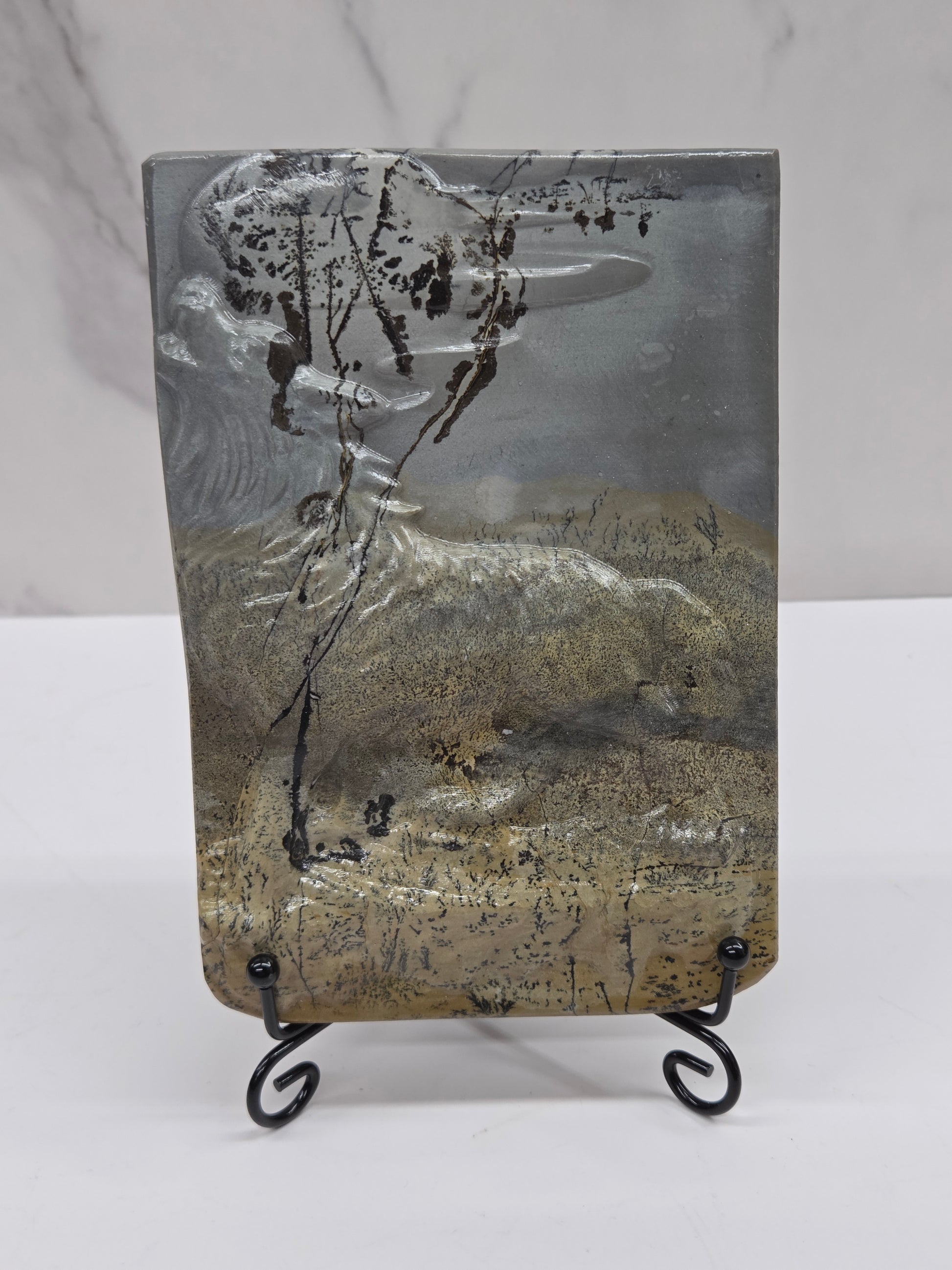 Picture Jasper slab with patterns and a wolf and moon carved into it, on a black stand against a white background
