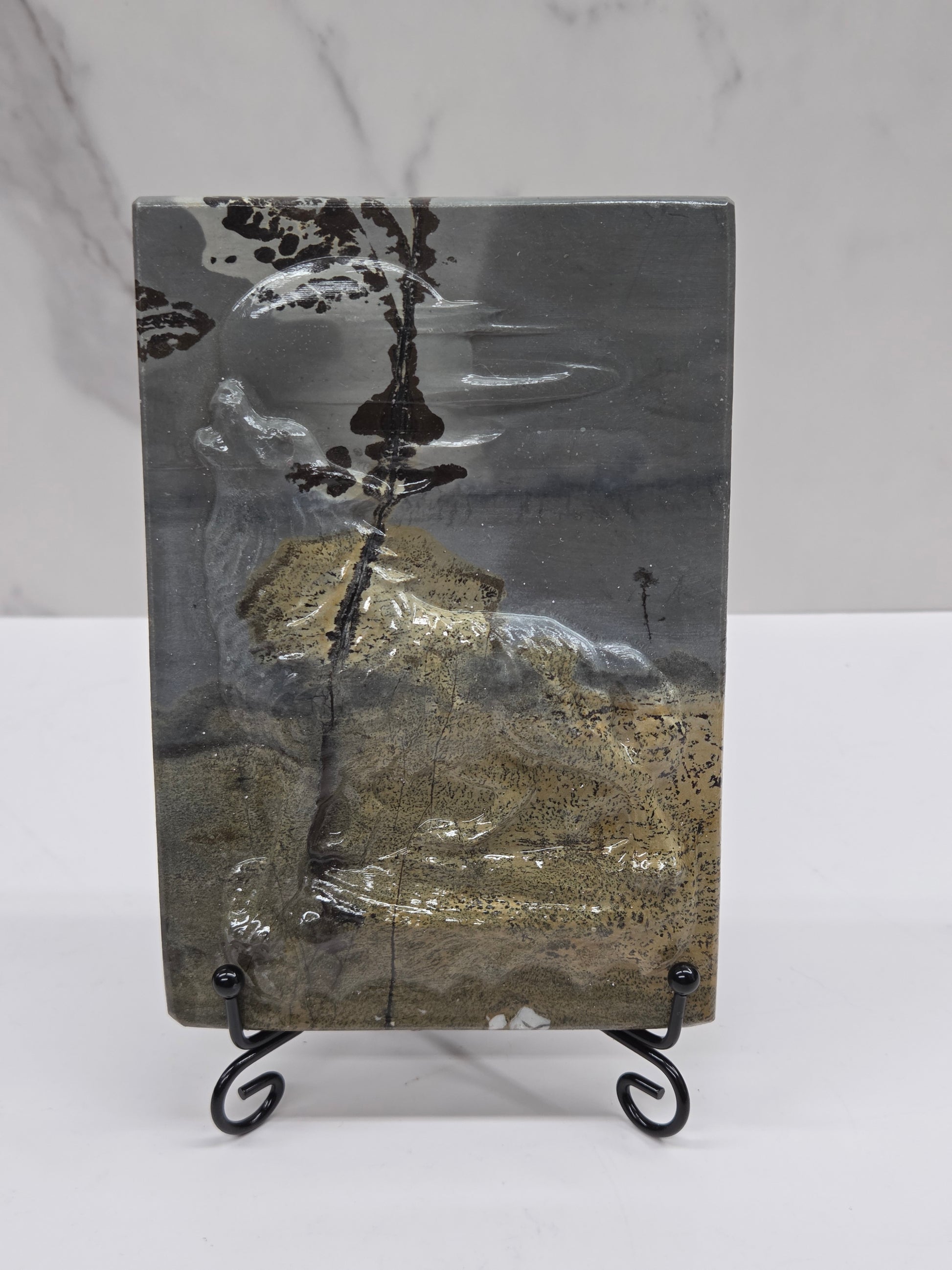 Picture Jasper slab with patterns and a wolf and moon carved into it, on a black stand against a white background