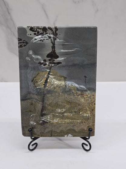 Picture Jasper slab with patterns and a wolf and moon carved into it, on a black stand against a white background