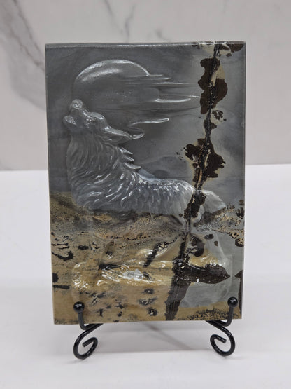 Picture Jasper slab with patterns and a wolf and moon carved into it, on a black stand against a white background