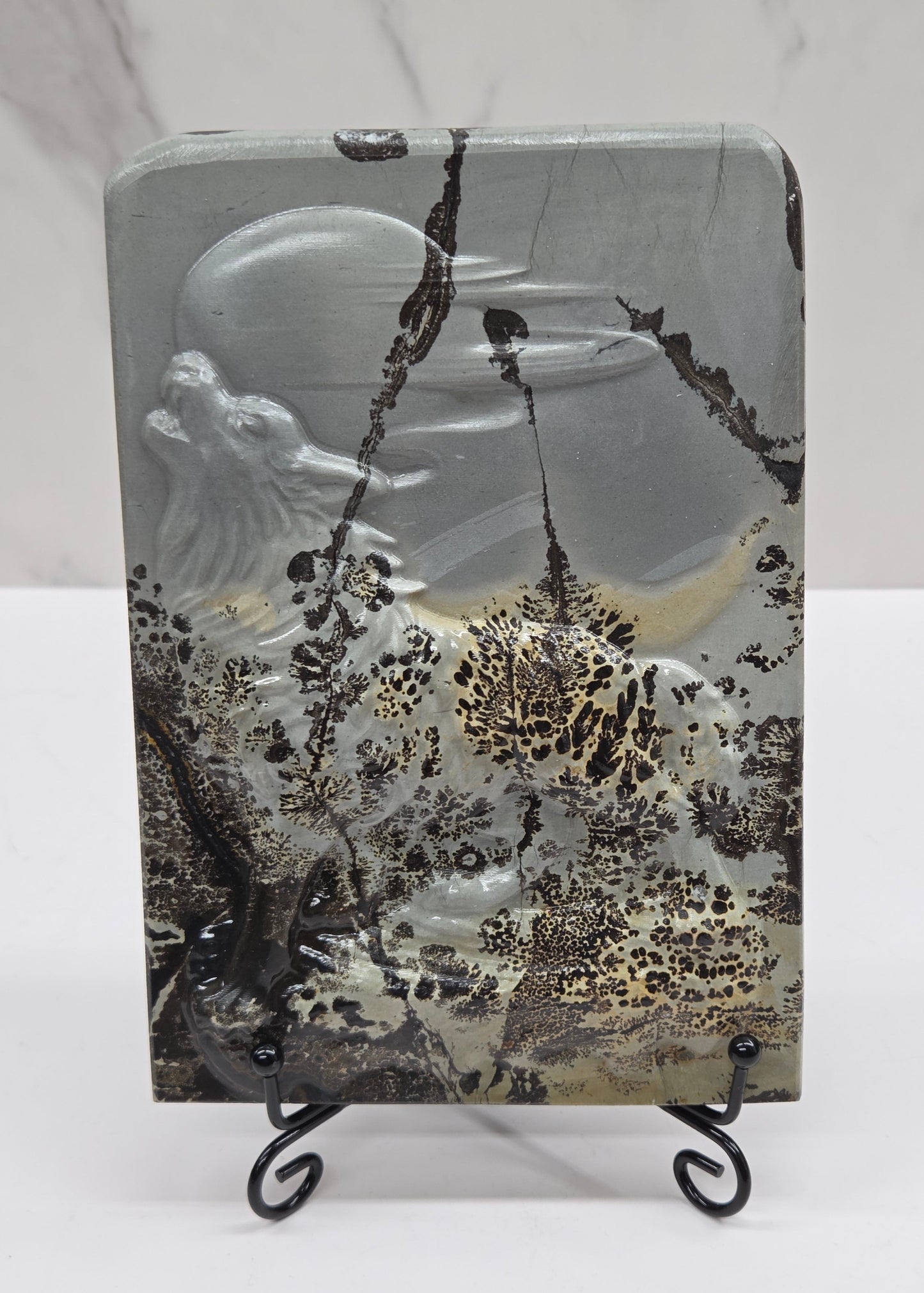 Picture Jasper slab with patterns and a wolf and moon carved into it, on a black stand against a white background