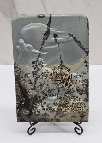 Picture Jasper slab with patterns and a wolf and moon carved into it, on a black stand against a white background