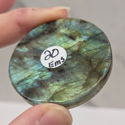 Round labradorite stone with a label held between fingers against a neutral background