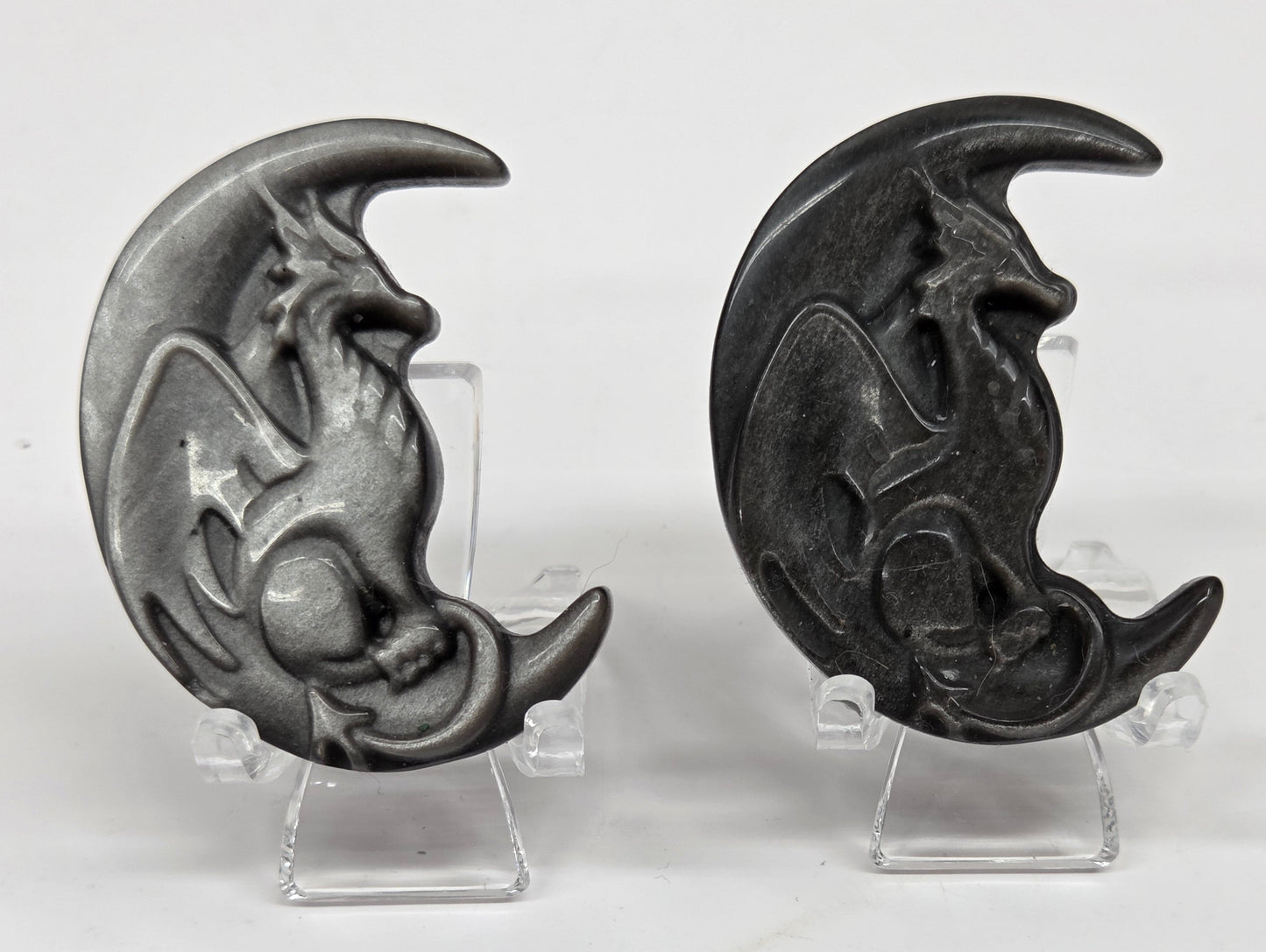 Two silver sheen obsidian dragon-shaped carvings on a white background