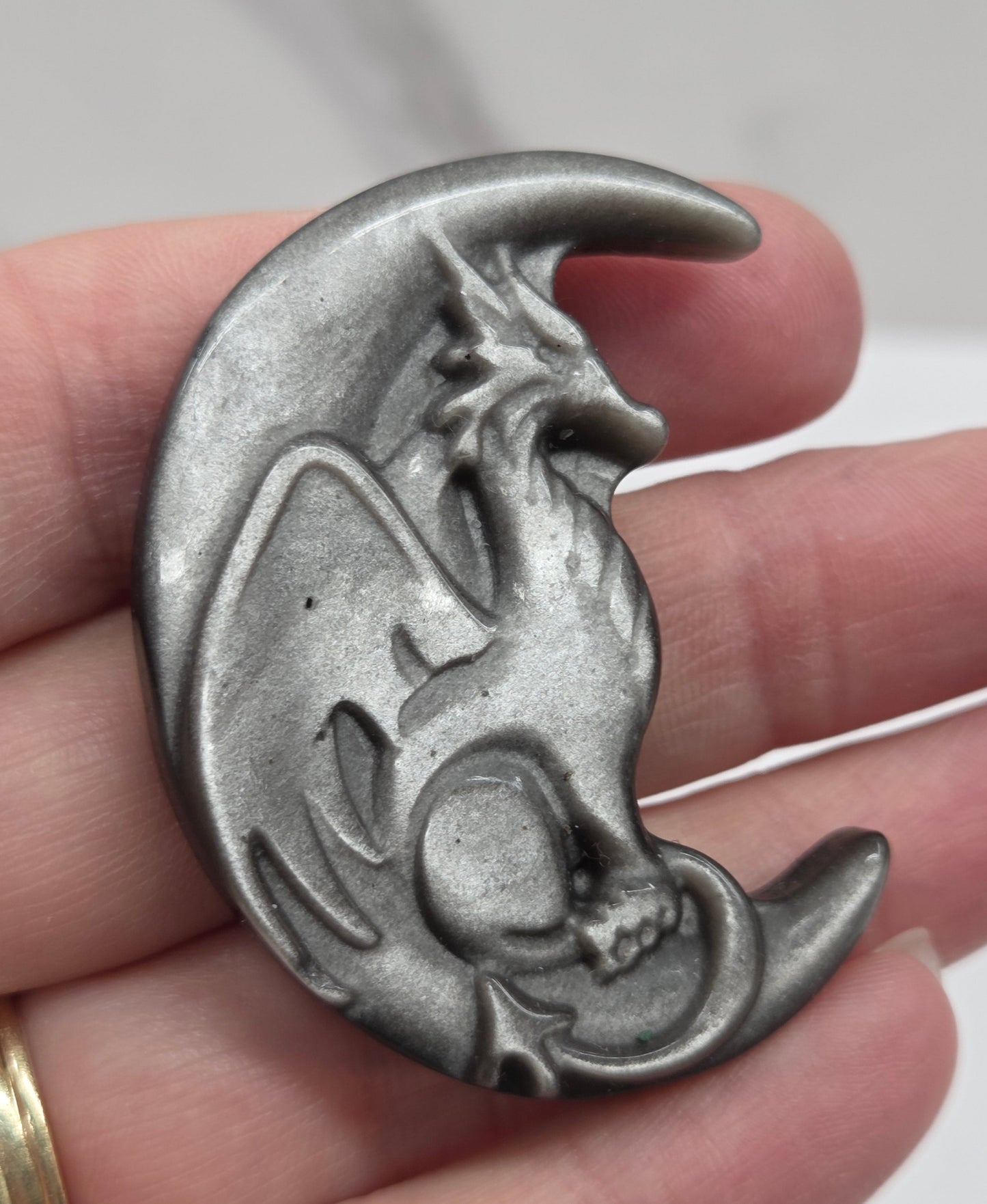 hand holding a silver sheen obsidian dragon-shaped carving on a white background