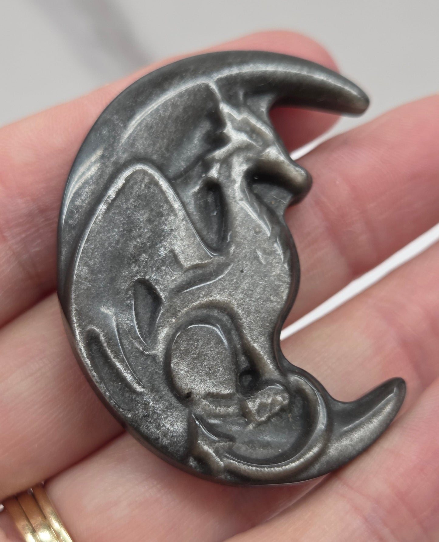 hand holding a silver sheen obsidian dragon-shaped carving on a white background
