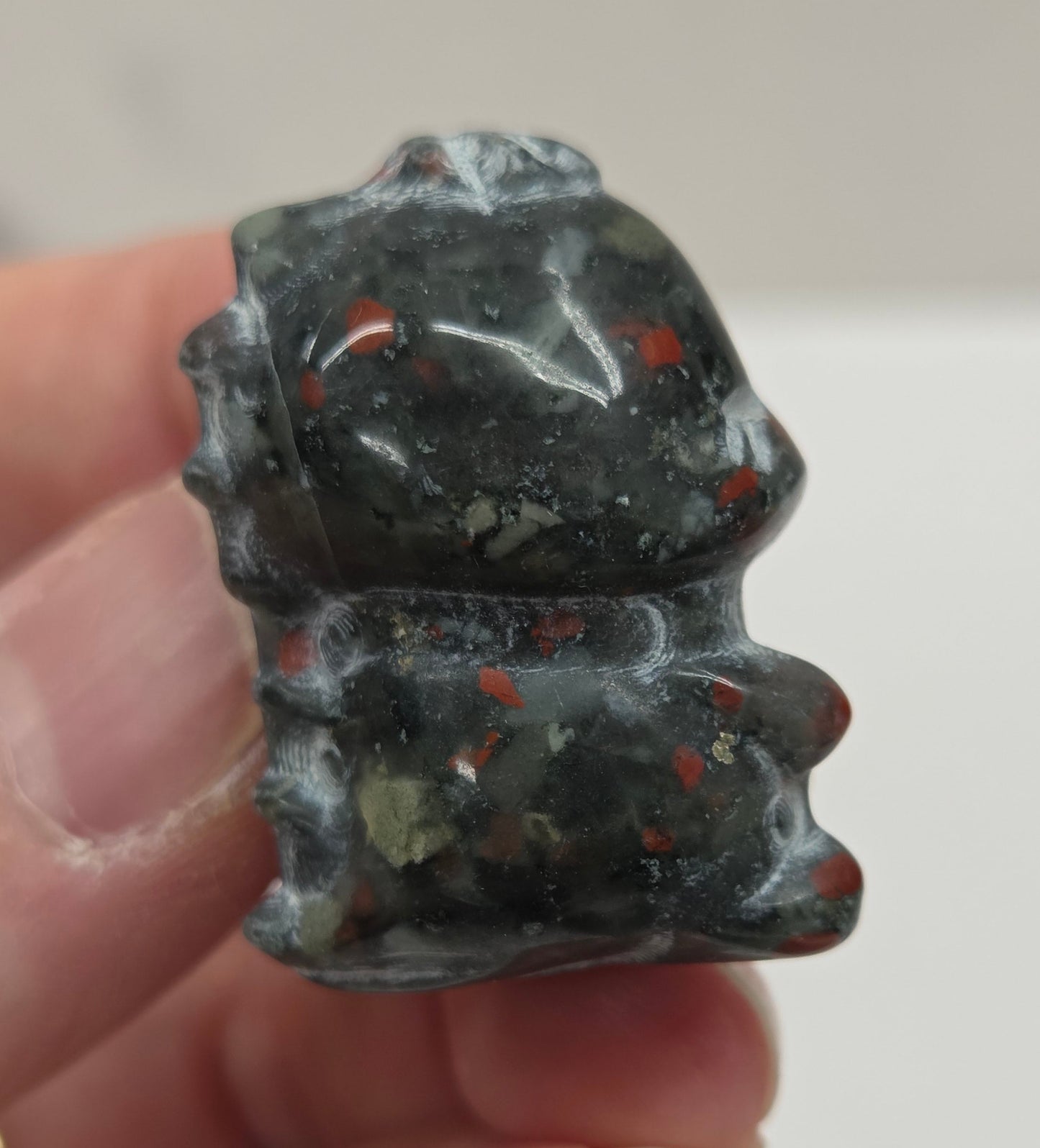 Hand holding an African Bloodstone cute dinosaur carving on a white background