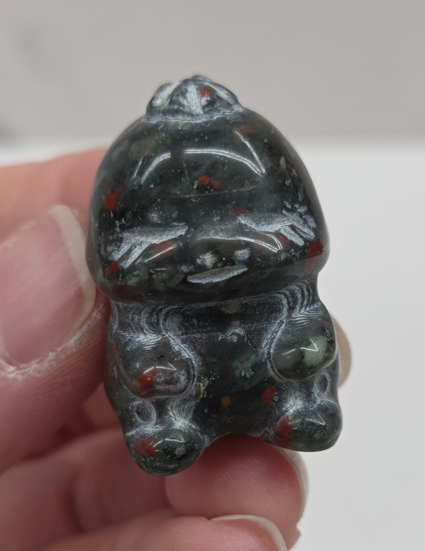 Hand holding an African Bloodstone cute dinosaur carving on a white background