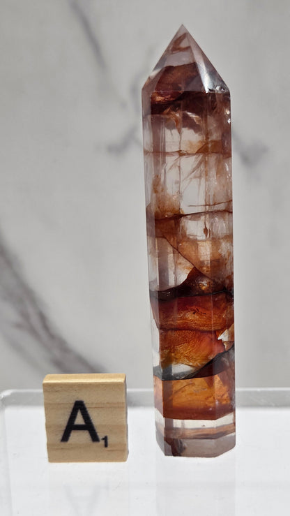 fire quartz crystal point on a white stand against a marble background
