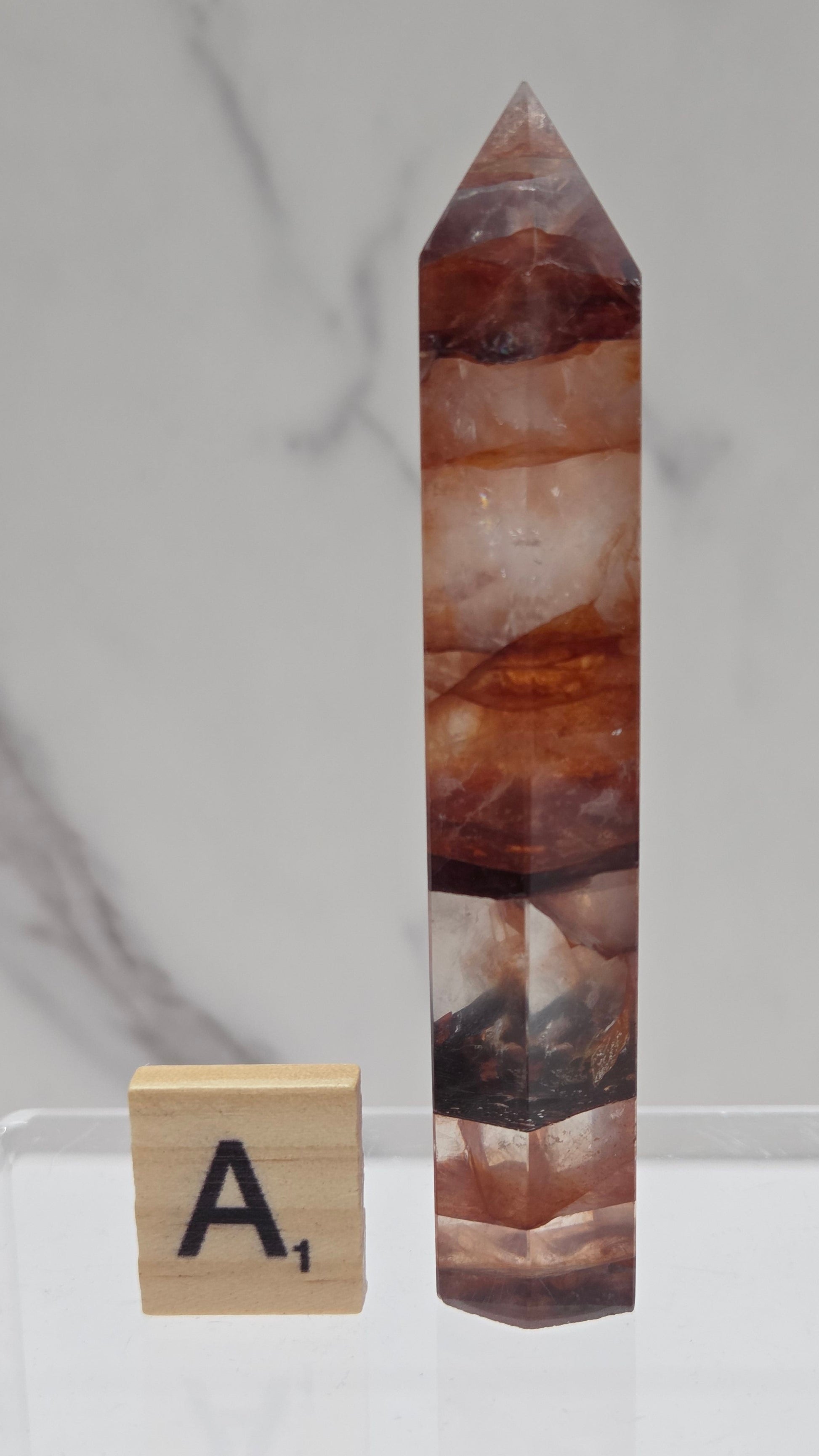 fire quartz crystal point on a white stand against a marble background