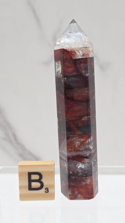 fire quartz crystal point on a white stand against a marble background