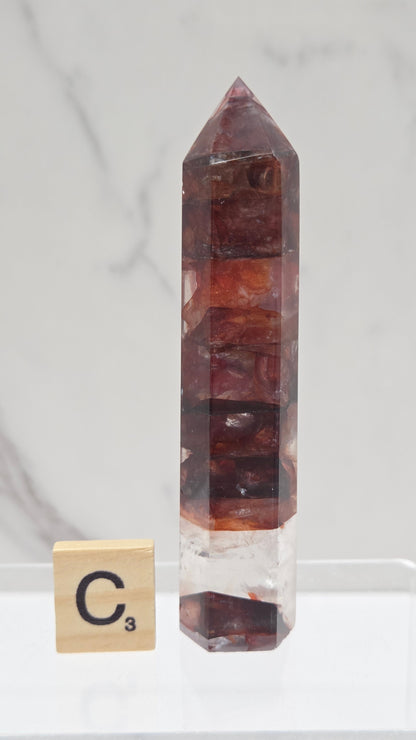fire quartz crystal point on a white stand against a marble background