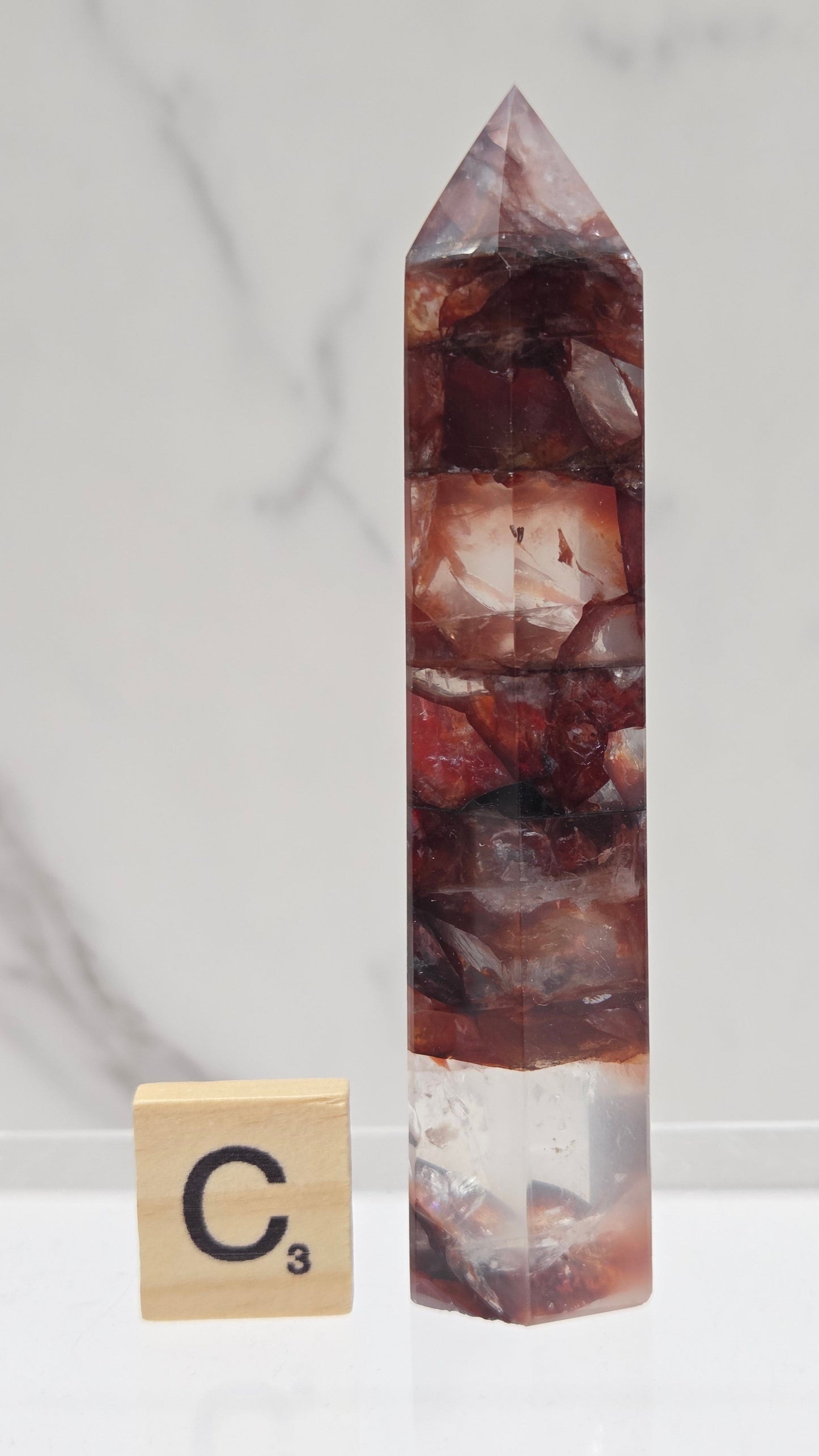 fire quartz crystal point on a white stand against a marble background