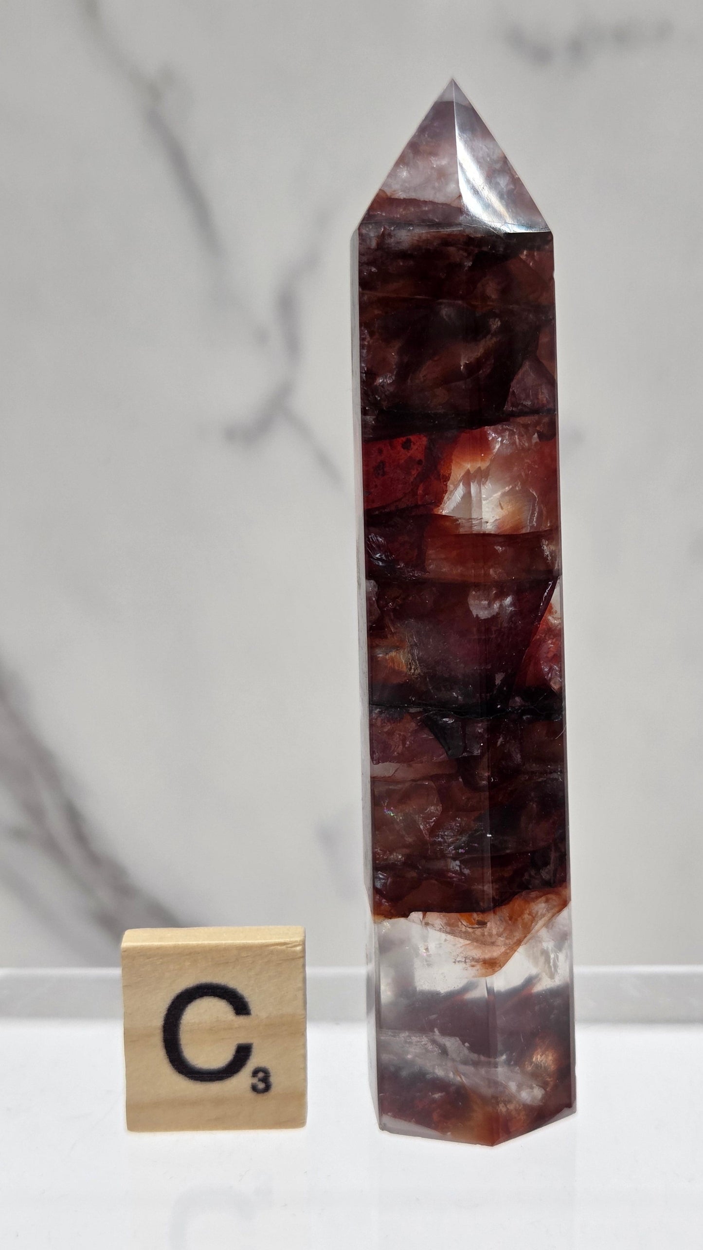fire quartz crystal point on a white stand against a marble background