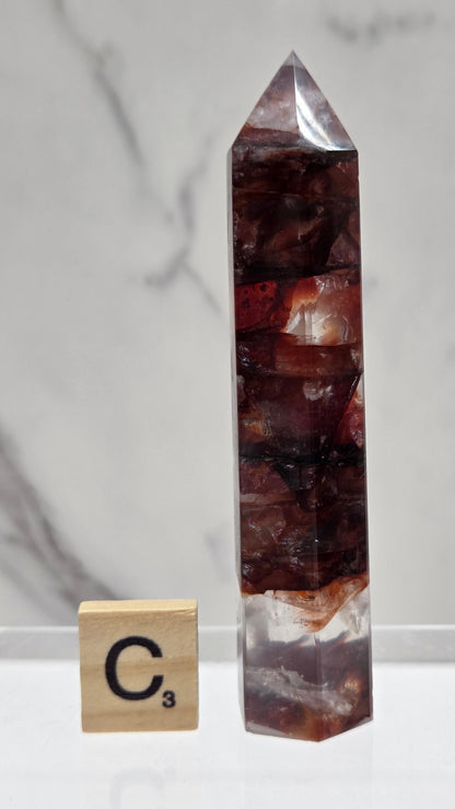 fire quartz crystal point on a white stand against a marble background