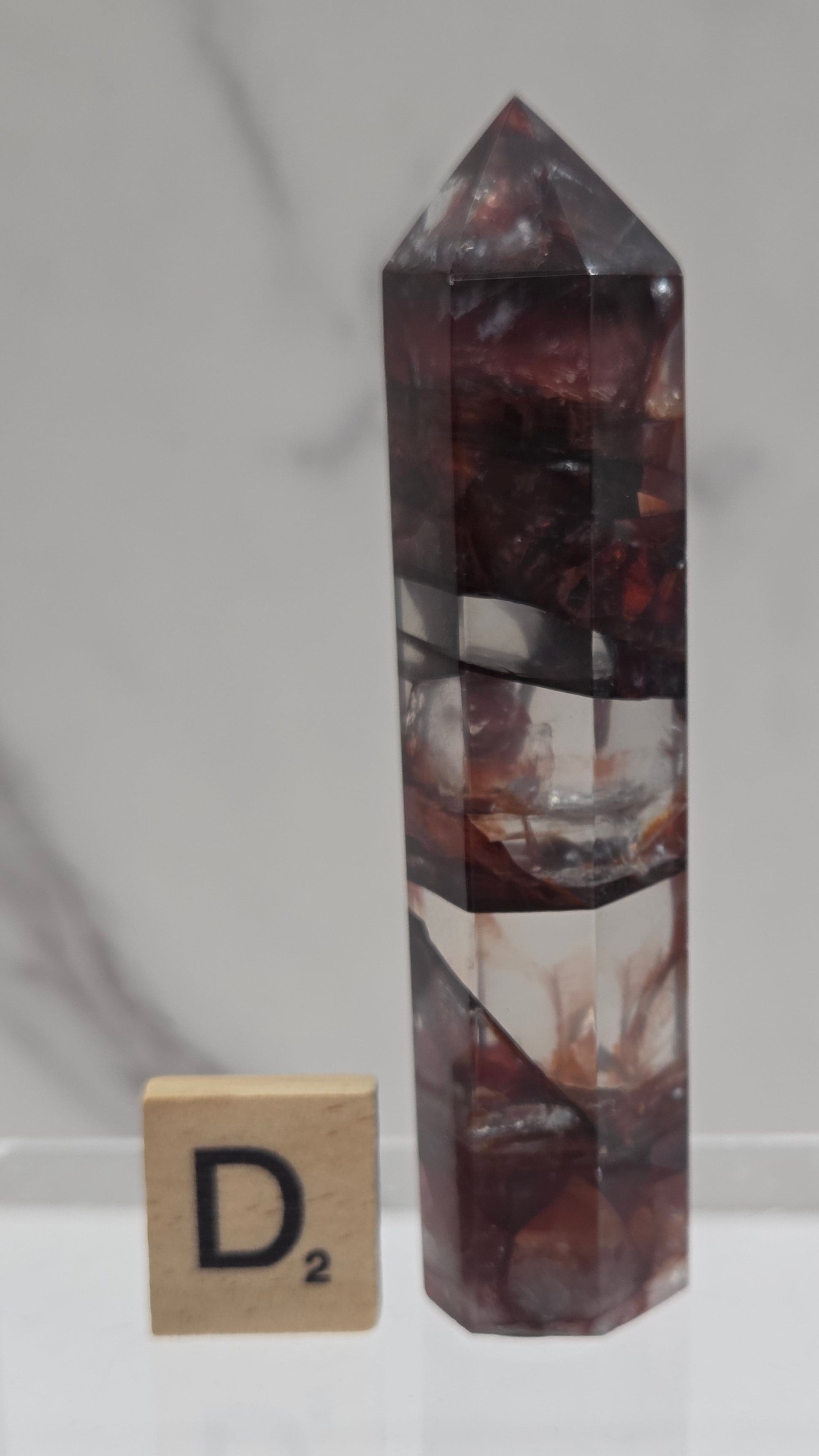 fire quartz crystal point on a white stand against a marble background