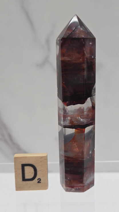 fire quartz crystal point on a white stand against a marble background