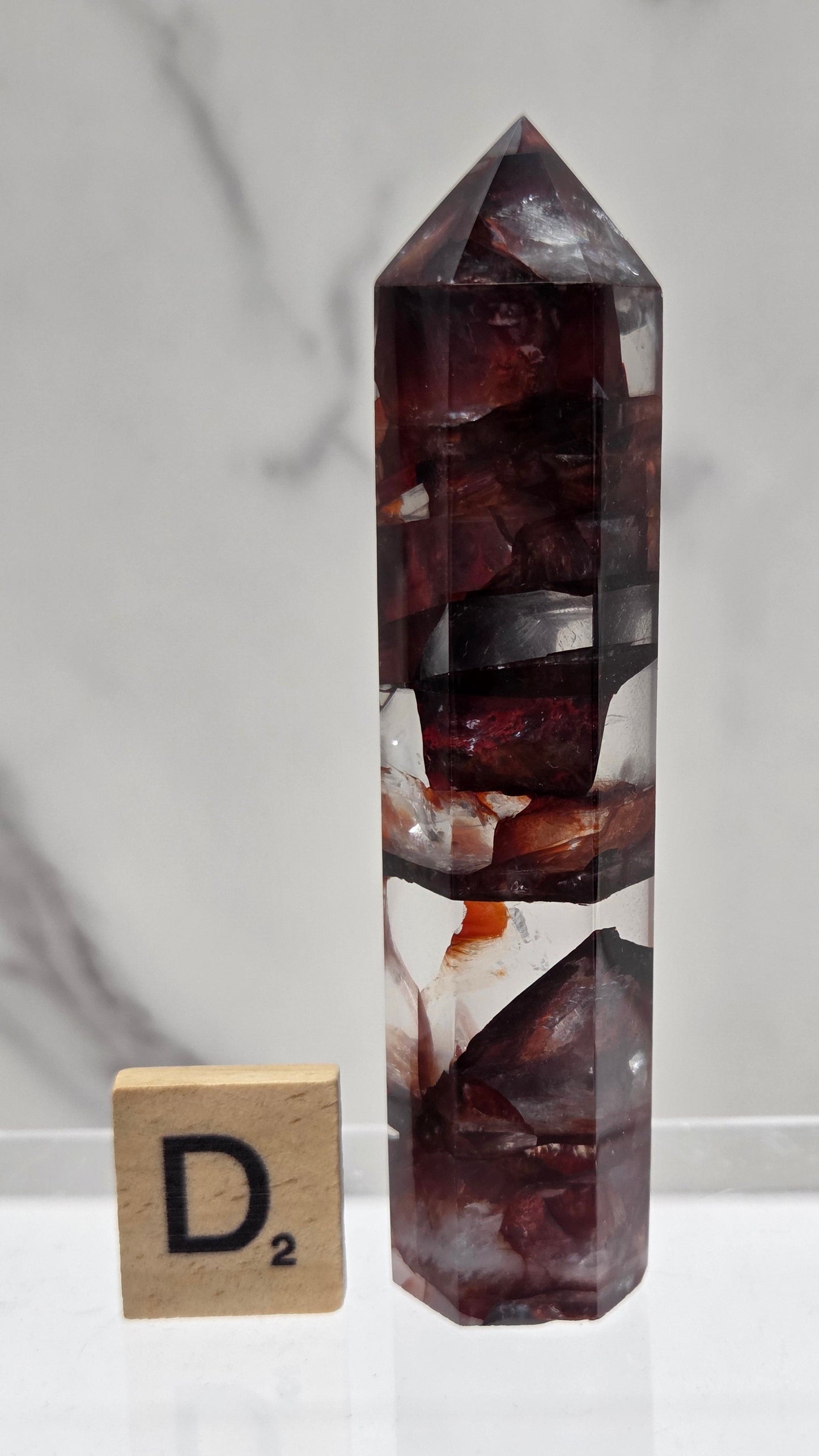 fire quartz crystal point on a white stand against a marble background