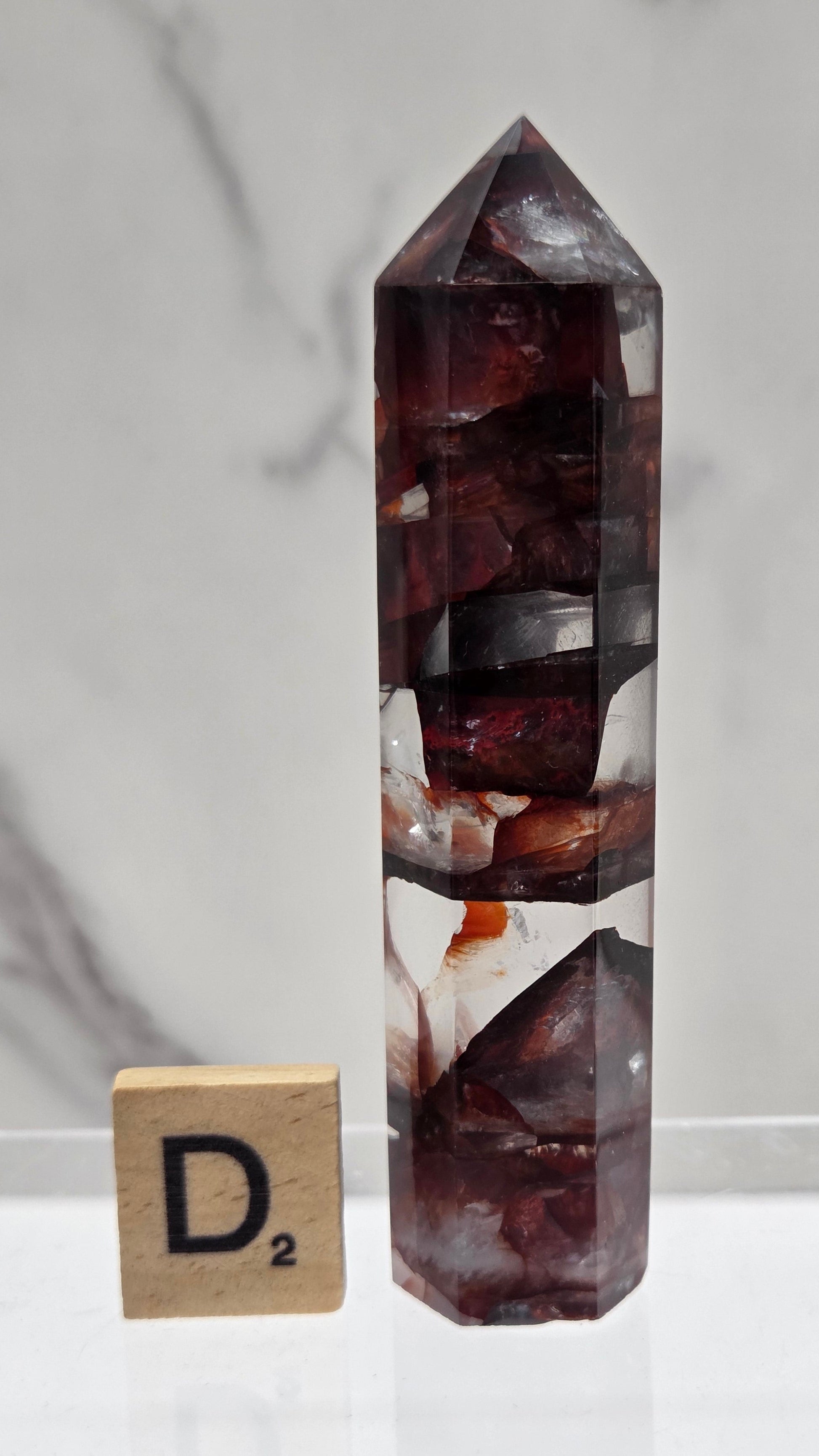 fire quartz crystal point on a white stand against a marble background