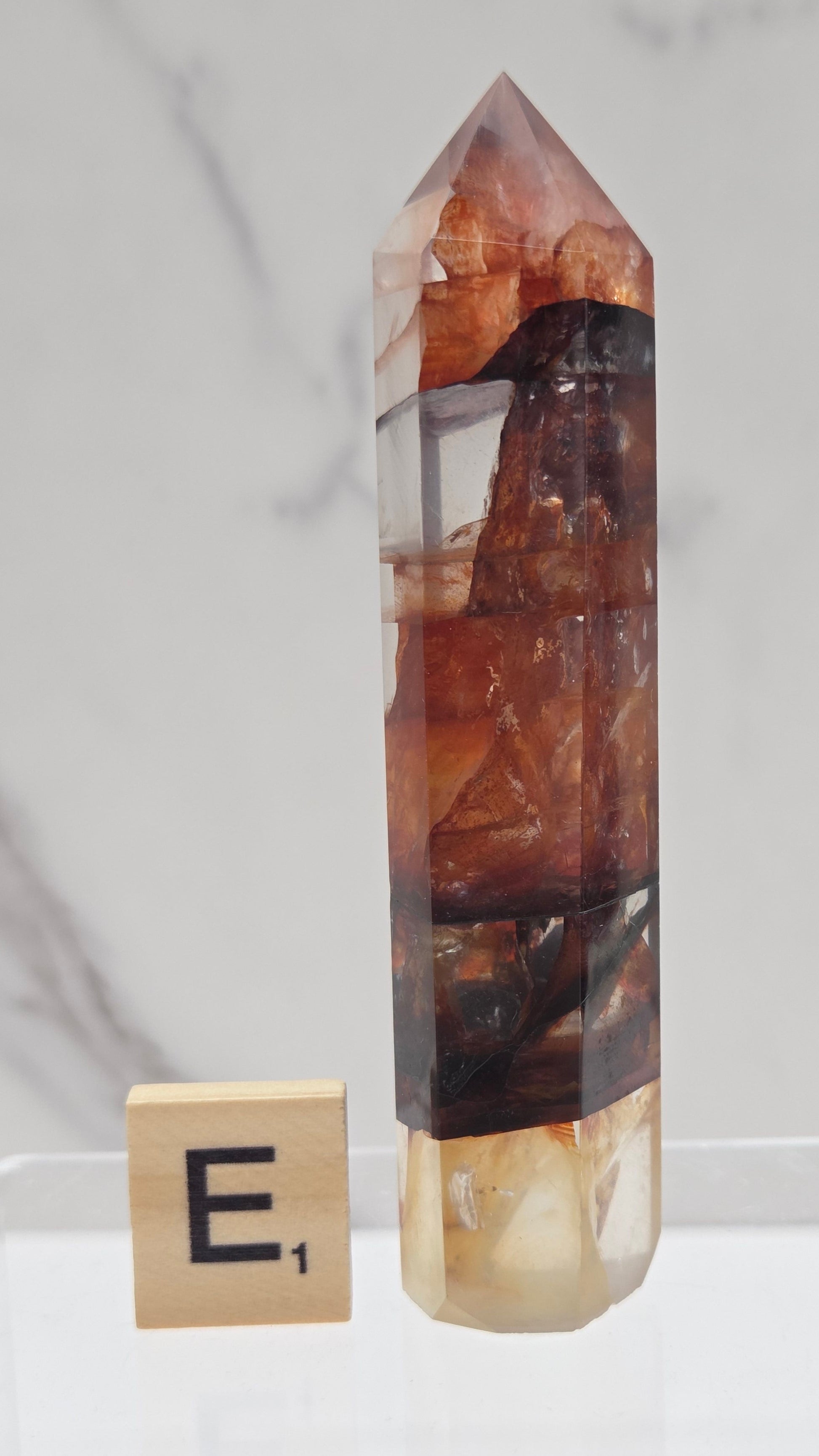 fire quartz crystal point on a white stand against a marble background