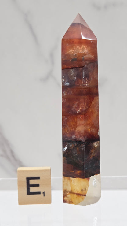 fire quartz crystal point on a white stand against a marble background