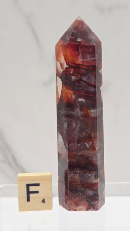 fire quartz crystal point on a white stand against a marble background