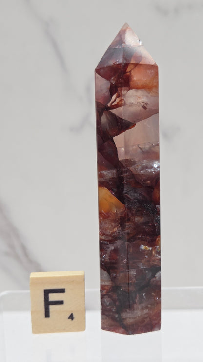 fire quartz crystal point on a white stand against a marble background
