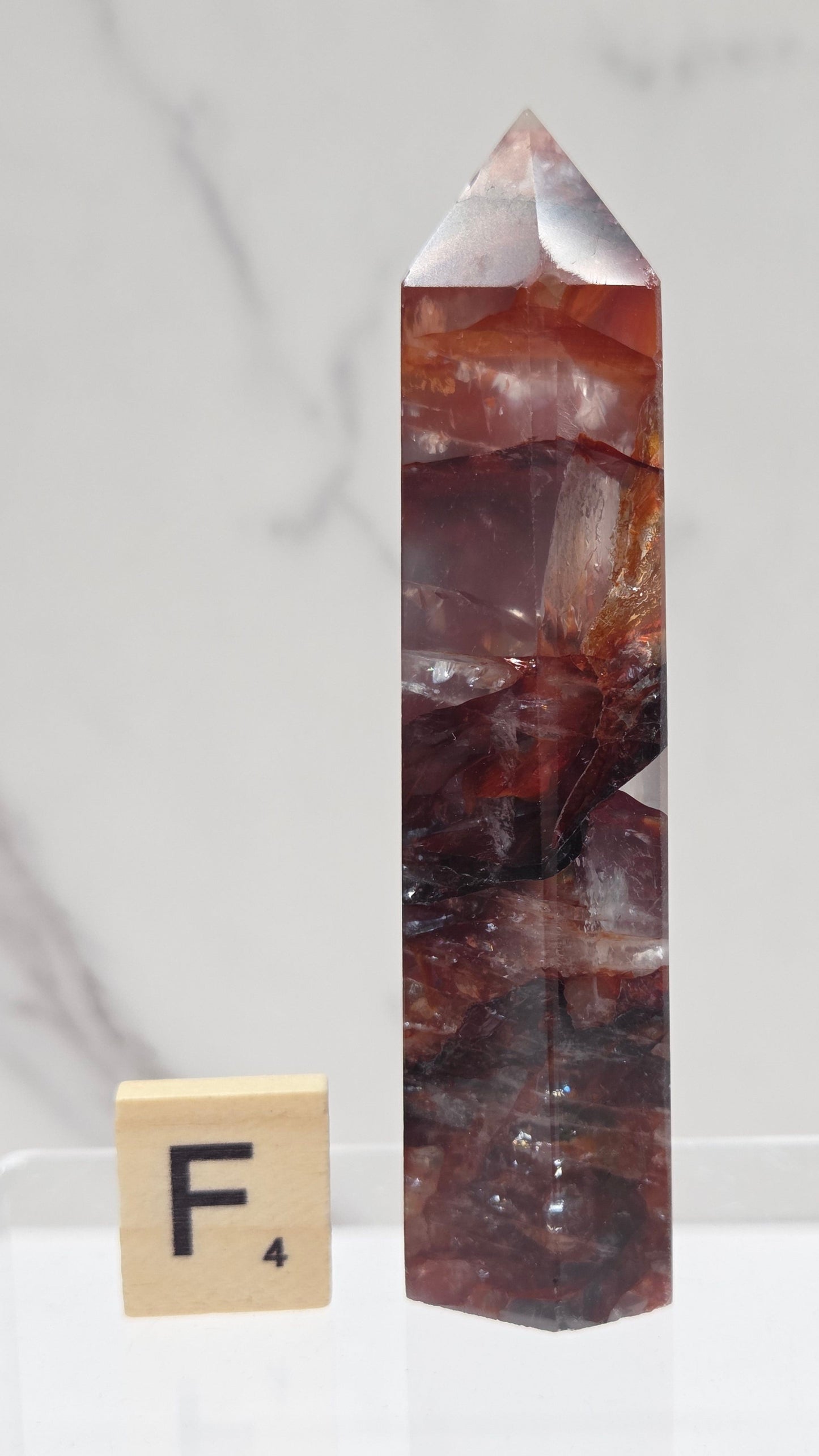 fire quartz crystal point on a white stand against a marble background