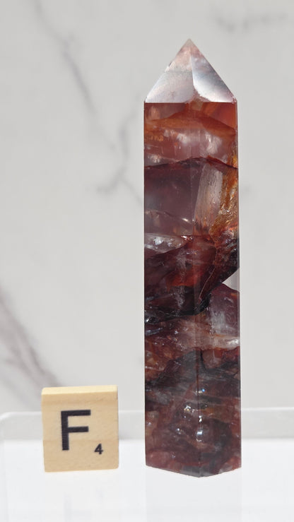 fire quartz crystal point on a white stand against a marble background