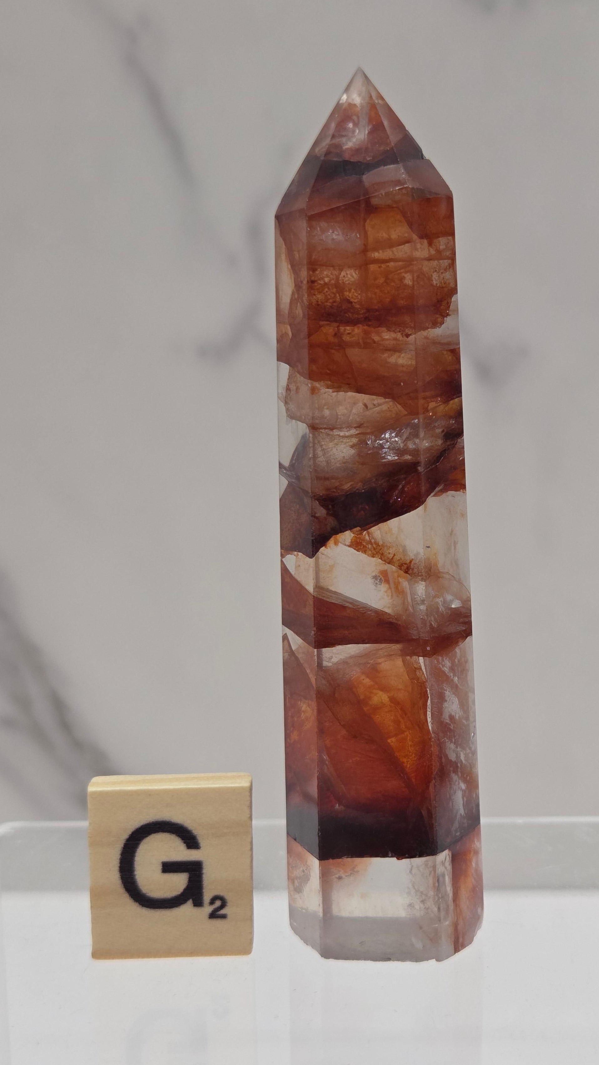 fire quartz crystal point on a white stand against a marble background