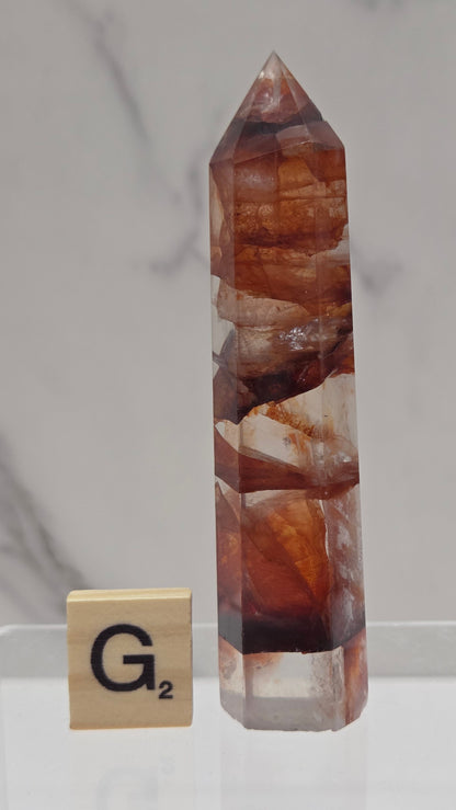 fire quartz crystal point on a white stand against a marble background