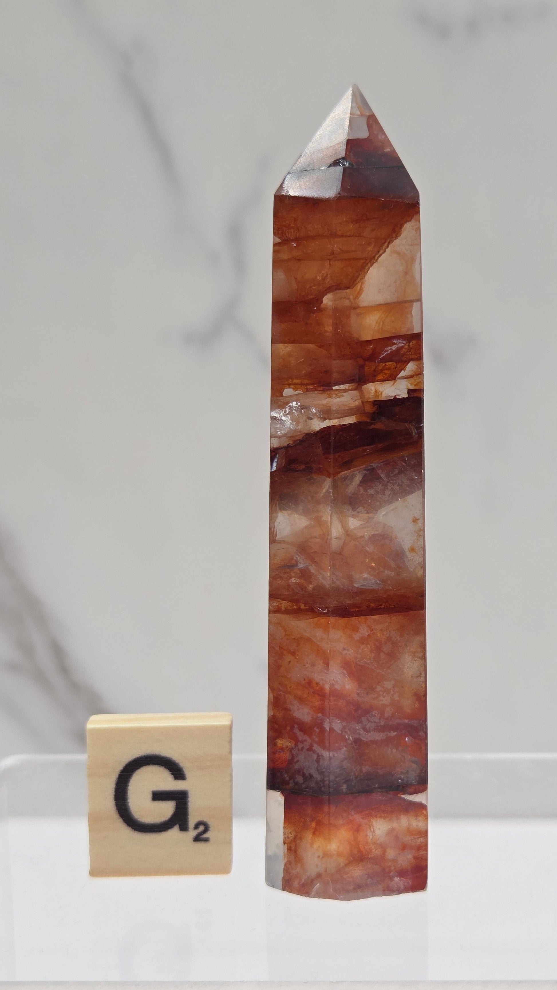 fire quartz crystal point on a white stand against a marble background